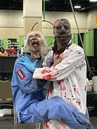 person in bloody white doc's coat holding zombie puppet